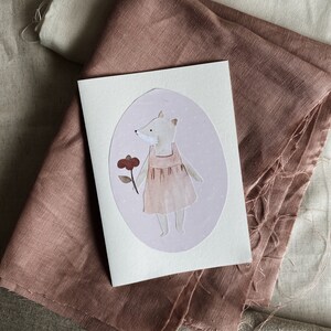 Puede incluir: Una tarjeta blanca con una ilustraci&oacute;n ovalada rosa de un zorro con un vestido rosa y sosteniendo una flor roja. El zorro est&aacute; de pie sobre un fondo rosa con lunares blancos.