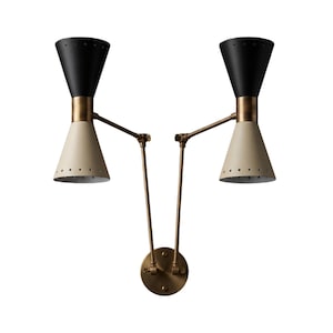 May include: A double-headed wall sconce with a mid-century modern design. The sconce features two cone-shaped shades, one black and one cream-colored, connected by adjustable brass arms to a circular base. The shades have small perforations.