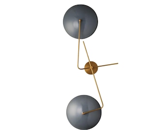May include: A wall-mounted light fixture featuring two circular, slate-gray shades attached to a central brass-colored metal frame. The structure consists of a central circular plate with thin, angular arms extending to support the two dome-shaped lights.