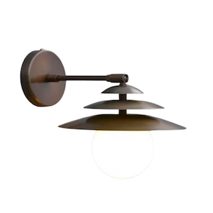 May include: A wall-mounted light fixture featuring a circular bronze backplate, a horizontal arm, and a tiered shade composed of three stacked, graduated bronze discs. A spherical white glass globe hangs beneath the shade to diffuse light.