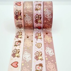 May include: Four rolls of washi tape with a pink and gold background. The tape features a repeating pattern of roses, gold glitter, and a couple of bears with the text "Be Mine".