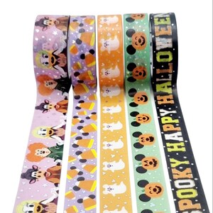 May include: Four rolls of Halloween themed washi tape. The first roll features a pink background with Mickey Mouse and friends dressed in Halloween costumes. The second roll features a purple background with orange and white candy corn. The third roll features an orange background with white ghosts. The fourth roll features a green background with Mickey Mouse wearing a pumpkin costume. The text on the fourth roll reads "Boo Spooky Happy Halloween".
