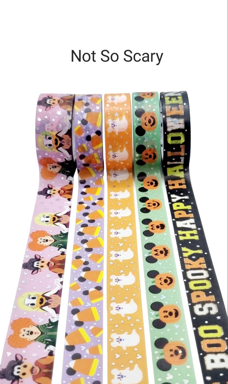 May include: Four rolls of Halloween themed washi tape. The first roll features a pink background with Mickey Mouse and friends dressed in Halloween costumes. The second roll features a purple background with orange and white candy corn. The third roll features an orange background with white ghosts. The fourth roll features a green background with Mickey Mouse wearing a pumpkin costume. The text on the fourth roll reads "Boo Spooky Happy Halloween".