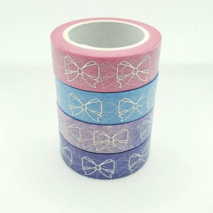 May include: Four rolls of washi tape with a white bow pattern on a light pink, light blue, purple, and dark blue background.
