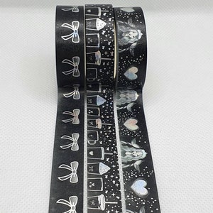 May include: Four rolls of black washi tape with silver holographic designs. The designs include bows, coffee cups, stars, and a woman with wings. The text "Midnight Cafe" is printed above the tape.