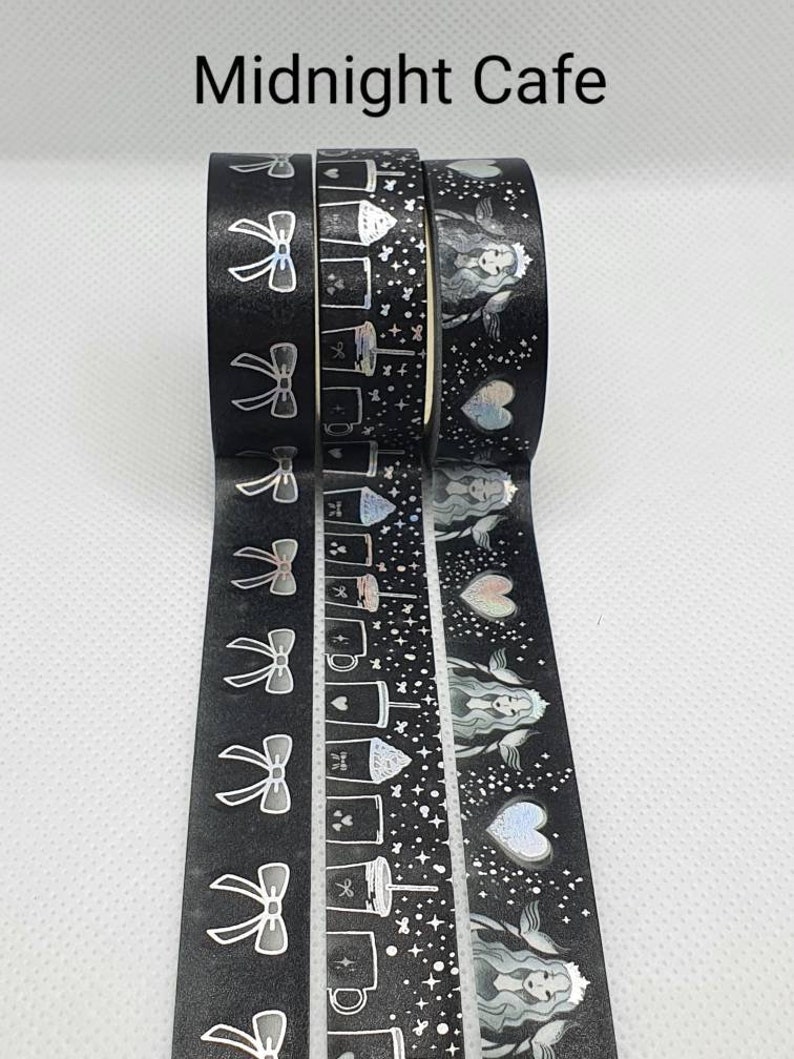 May include: Four rolls of black washi tape with silver holographic designs. The designs include bows, coffee cups, stars, and a woman with wings. The text "Midnight Cafe" is printed above the tape.