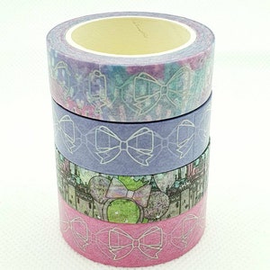 Può includere: Quattro rotoli di nastro washi con uno schema di colori pastello. Il nastro presenta un motivo ripetitivo di fiocchi bianchi su uno sfondo lilla chiaro, blu, verde e rosa.