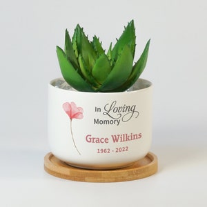 May include: White ceramic planter with a green succulent plant, a pink flower design, and the text "In Loving Memory Grace Wilkins 1962 - 2022".