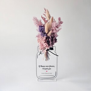 May include: A clear acrylic vase with a mason jar design, filled with a bouquet of dried flowers in shades of pink and purple. The vase has a quote that reads "If humans were flowers, I'd pick you" with a small red heart. The vase is on a white background.
