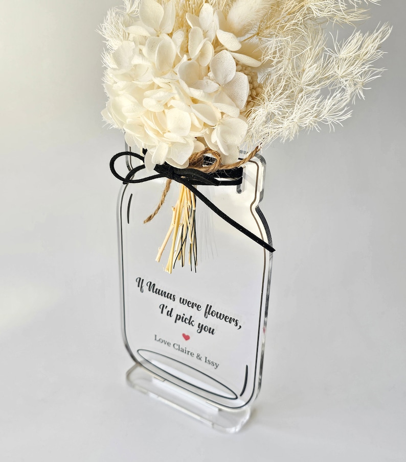 May include: A clear acrylic vase shaped like a mason jar with a black ribbon and dried white flowers. The vase has a white label with the text "If Nanas were flowers, I'd pick you" and a red heart. The label also includes the text "Love Claire & Issy".