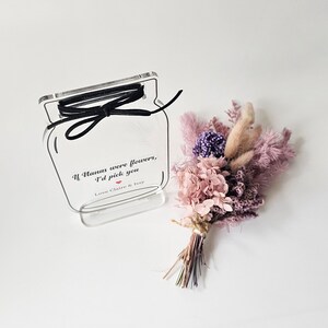 May include: A clear acrylic jar with a black ribbon tied around the top. The jar has a printed message that reads "If humans were flowers, I'd pick you. Love Claire & Issy". A small bouquet of dried flowers in shades of pink and purple is next to the jar.