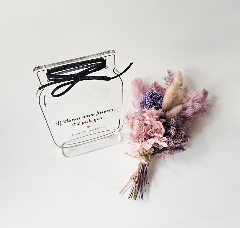 May include: A clear acrylic jar with a black ribbon tied around the top. The jar has a printed message that reads "If humans were flowers, I'd pick you. Love Claire & Issy". A small bouquet of dried flowers in shades of pink and purple is next to the jar.