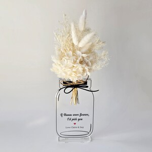 May include: White dried flower arrangement in a clear glass jar with a black ribbon and a white background. The jar has a black outline and the text "If humans were flowers, I'd pick you Love Claire & Issy" with a red heart.