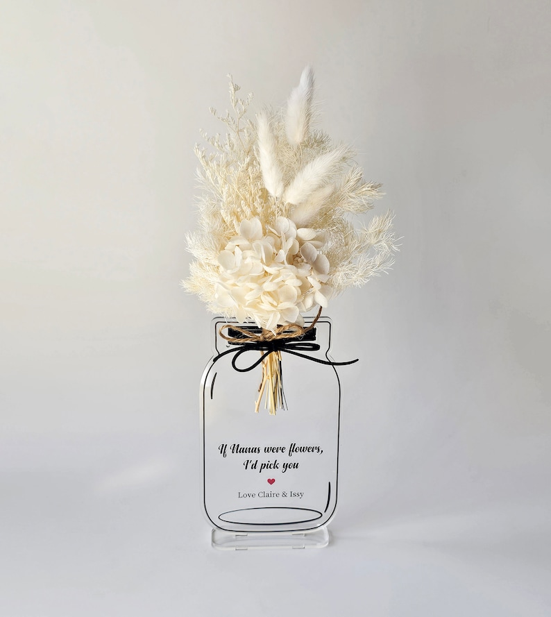 May include: White dried flower arrangement in a clear glass jar with a black ribbon and a white background. The jar has a black outline and the text "If humans were flowers, I'd pick you Love Claire & Issy" with a red heart.