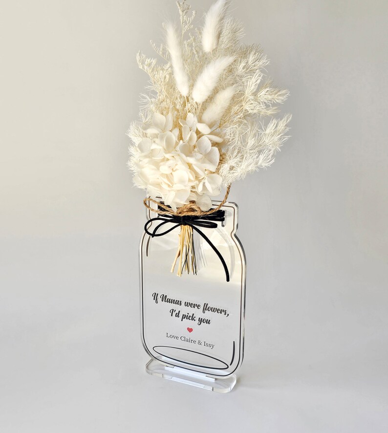 May include: White dried flowers in a clear acrylic mason jar with a black ribbon and the text "If humans were flowers, I'd pick you Love Claire & Issy"