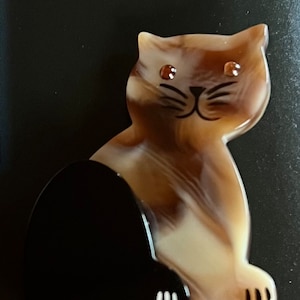 May include: A black and white striped cat figurine with brown and white marbled fur. The cat has brown eyes and a black nose.