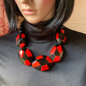 Puede incluir: Un collar de declaración geométrico negro y rojo. El collar está hecho de cuentas grandes, facetadas, de forma ovalada.