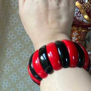 May include: A red and black bangle bracelet with a glossy finish. The bracelet is made of multiple stacked rings of red and black plastic.