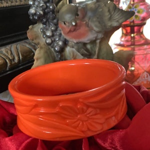 Könnte beinhalten: Hellorangefarbene Keramik-Schmuckschale mit floralem Design. Die Schale ist oval und steht auf einer roten Satin-Oberfläche. Die Schale hat ein erhabenes Blumenmuster an den Seiten.