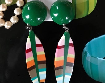 May include: A pair of green and multi-colored dangle earrings with a green round top. The earrings are on a white card with the text "Marion Godart".