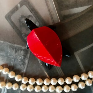 Puede incluir: Una figurita de tortuga roja y negra con un collar de perlas en primer plano.