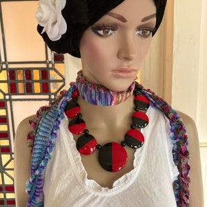 May include: A mannequin wearing a white tank top with a black and red statement necklace. The necklace is made of large, round, black and red plastic beads. The mannequin is also wearing a colorful scarf around her neck.