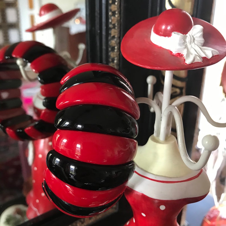 May include: A red and black striped plastic bangle bracelet. The bracelet is made of multiple stacked rings of red and black plastic.