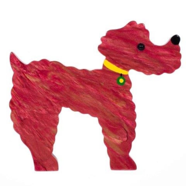 May include: A red wooden dog figurine with a yellow collar and a green and yellow tag. The dog has black eyes and a black nose. The figurine is standing on a white background.
