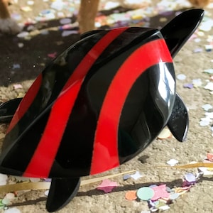 Puede incluir: Una figurita de tortuga rayada de negro y rojo. La tortuga está hecha de plástico y tiene un acabado brillante.