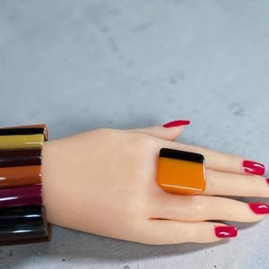 May include: A multi-coloured bracelet composed of stacked, smooth, rectangular segments in shades of black, mustard yellow, dark brown, rust orange, and deep plum, paired with a matching ring featuring a two-tone black and orange square face.