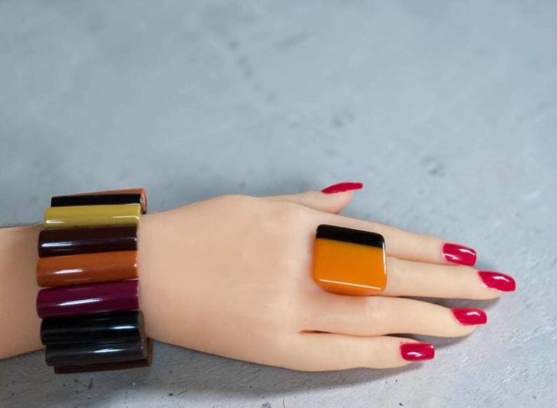 May include: A multi-coloured bracelet composed of stacked, smooth, rectangular segments in shades of black, mustard yellow, dark brown, rust orange, and deep plum, paired with a matching ring featuring a two-tone black and orange square face.