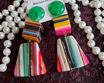 May include: Bright Marion Godart earrings with green, yellow, pink, and black details. The earrings feature a geometric design with rectangular and trapezoid shapes. A white tag with the brand name is visible.