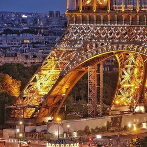 May include: A nighttime view of the Eiffel Tower in Paris, France. The tower is illuminated with golden lights, and the city lights can be seen in the background. A carousel is in the foreground, with people walking around it.