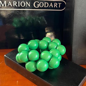 May include: A green wooden sculpture of a cluster of spheres, resembling a bunch of grapes. The sculpture is displayed on a black wooden base.