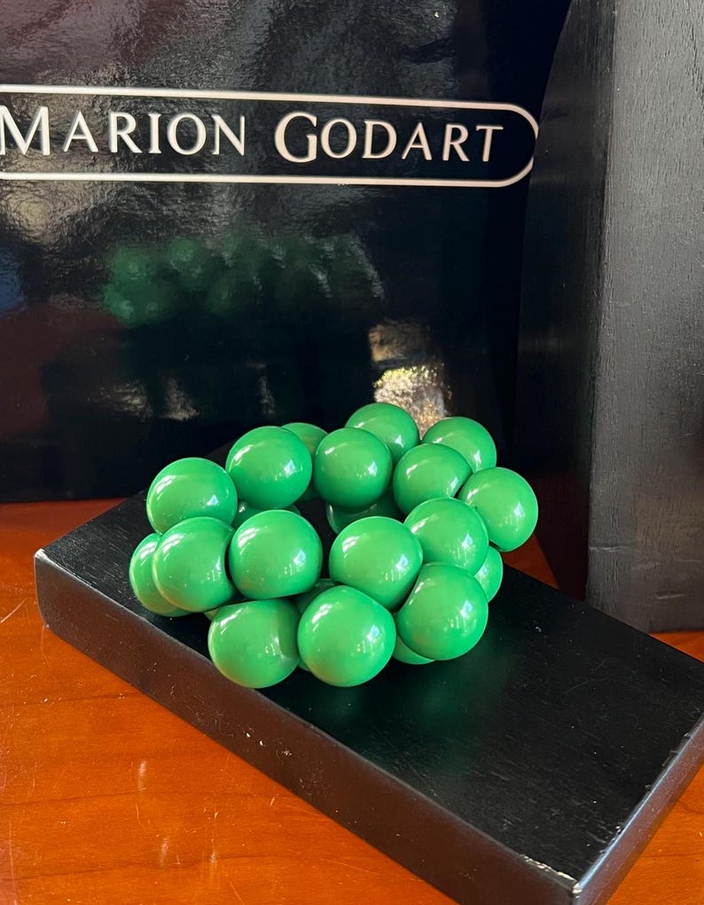 May include: A green wooden sculpture of a cluster of spheres, resembling a bunch of grapes. The sculpture is displayed on a black wooden base.