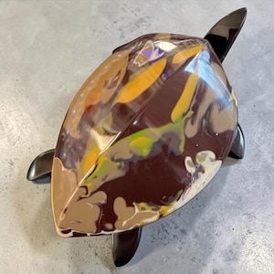 May include: A turtle-shaped sculpture featuring a glossy, dark brown shell with marbled swirls of yellow, light green, beige, and white. The head and four flippers are a solid, smooth, dark brown finish, contrasting with the multi-colored shell.
