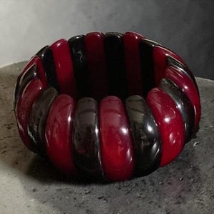 May include: A stretch bracelet composed of alternating smooth, rounded segments in deep glossy black and rich translucent dark red. The circular accessory features a repeating pattern of these polished, curved pieces arranged in a continuous band.