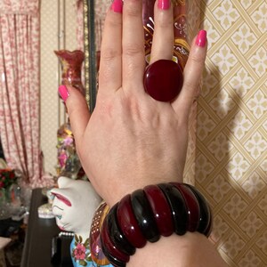 May include: A large, round, deep red ring with a smooth, glossy finish and a wide, segmented bangle bracelet featuring alternating vertical bands of polished black and deep red resin, creating a bold, high-contrast look on the wrist.