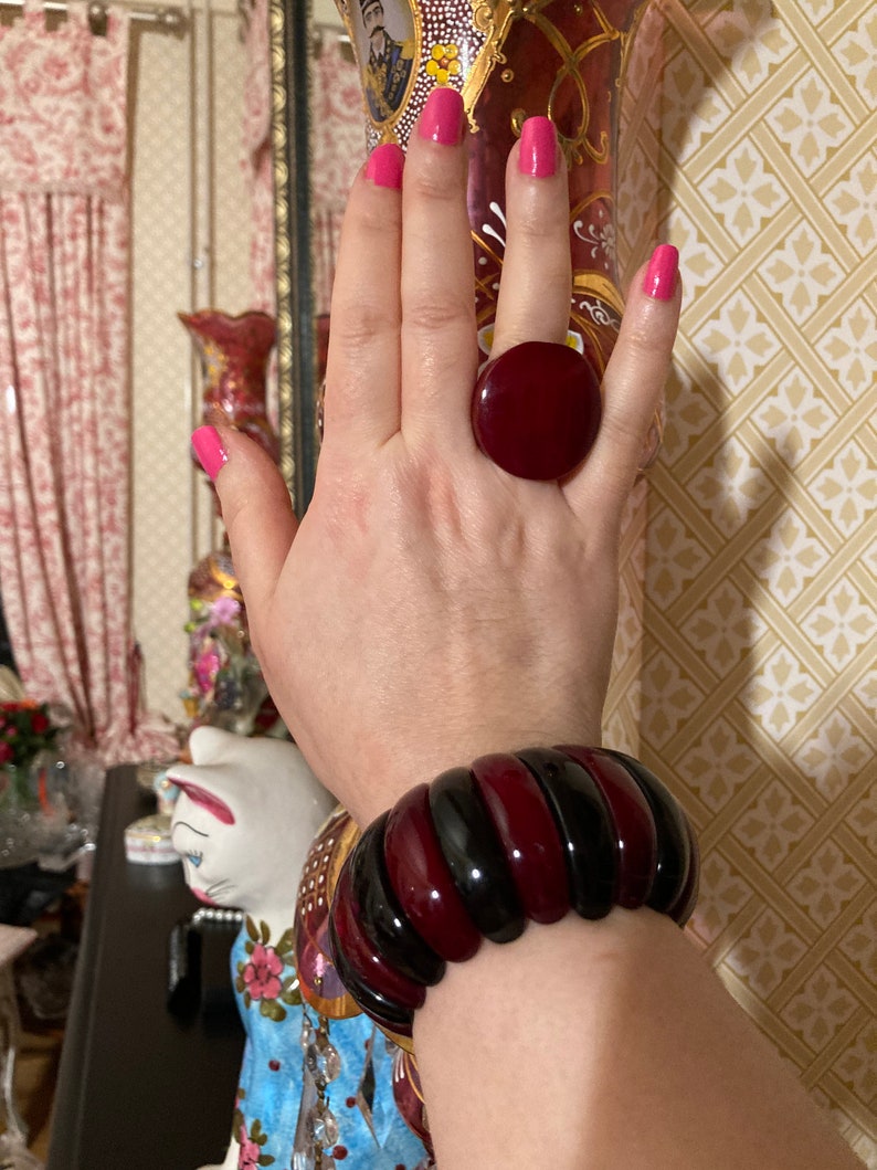 May include: A large, round, deep red ring with a smooth, glossy finish and a wide, segmented bangle bracelet featuring alternating vertical bands of polished black and deep red resin, creating a bold, high-contrast look on the wrist.