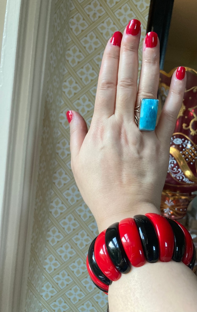 May include: A red and black bangle bracelet with a glossy finish. The bracelet is made of multiple stacked rings of red and black plastic.