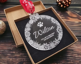 May include: A clear glass Christmas bauble with a white snowflake design and the name "Wilson" inscribed. The bauble also includes a paw print and the text "You left a paw print on our hearts".