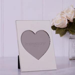 May include: White photo frame with a silver border and a heart-shaped opening. The frame says "Impressions Photo Frame" on the front.