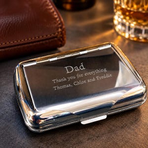May include: A rectangular, polished silver-tone metal case with a hinged lid. The lid is engraved with the text: Dad, Thank you for everything, Thomas, Chloe and Freddie. The case features a smooth, reflective surface and a secure latch closure.