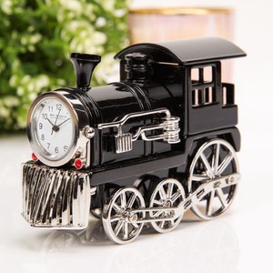 May include: A black train-shaped clock with a silver clock face and wheels. The clock face shows the time with black numerals and hands. The train has a decorative silver front and a small smokestack.