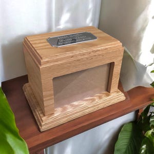 May include: A wooden box with a photo frame and a silver plaque that reads "Sarah Griffin 1957-2023 Loving Mom, Grandma & Wife".