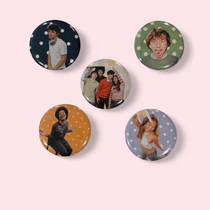 May include: A collection of five round pinback buttons. Each button features a different image of people. The buttons have various background colors, including navy, green, orange, and light blue, with white polka dots.