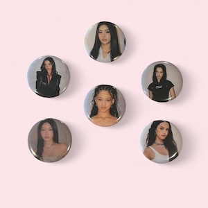 May include: A collection of six round buttons featuring portraits of women. The buttons have a glossy finish and are arranged on a light pink background. Each button displays a different woman with various hairstyles and outfits.