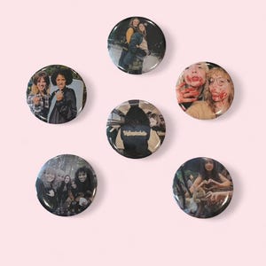 May include: A collection of six round pinback buttons with various images. The buttons feature photographs of people, including group shots and close-ups. The buttons are black with glossy surfaces, set against a light pink background.