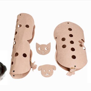 Peut inclure: Deux griffoirs à chat en carton brun avec des trous et une découpe en forme de visage de chat. Les poteaux sont en forme de cylindre et de rectangle arrondi. Deux chats sont assis de chaque côté des poteaux.