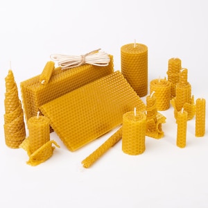 Può includere: Una collezione di candele di cera d'api naturale in varie forme e dimensioni, tra cui un foglio di favo, un blocco di cera d'api e un rotolo di spago. Le candele sono di colore giallo chiaro e hanno un aspetto naturale e rustico.